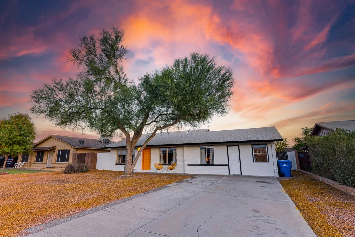 The home’s front porch area with comfortable chairs beneath a large tree, set against a colorful sky. The atmosphere is welcoming, inviting guests to relax, sip coffee, or enjoy casual outdoor conversations.