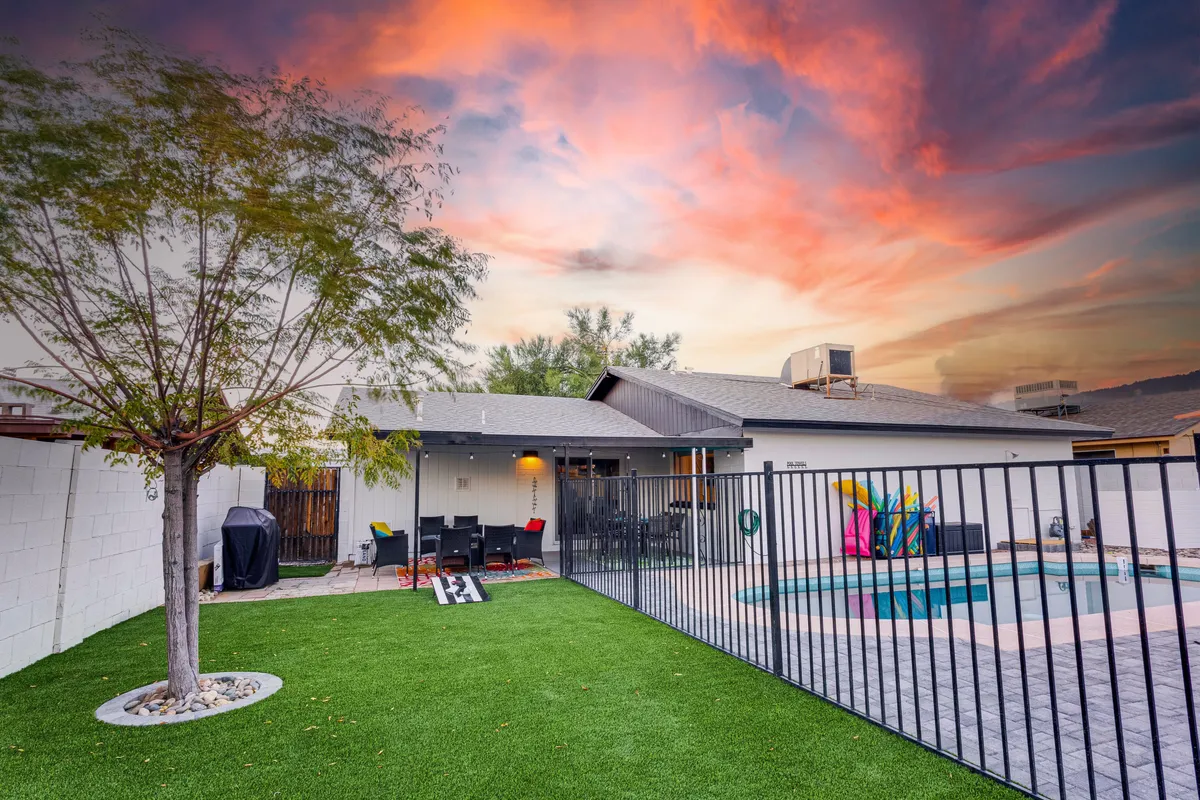A cheerful backyard scene featuring a sparkling swimming pool, outdoor seating area, and a lush tree providing shade. The space is designed for barbecuing, relaxing, and socializing, making it ideal for group get-togethers and continued fun after local entertainment.