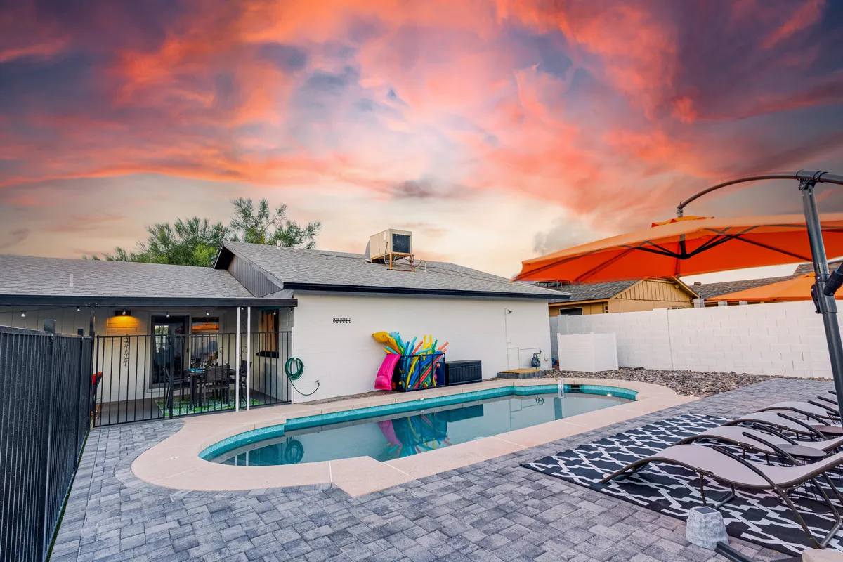 A playful view of the backyard featuring the swimming pool with colorful floats, an outdoor seating area, and a bright orange umbrella. The setup encourages sunbathing, casual dining, and playful pool activities.