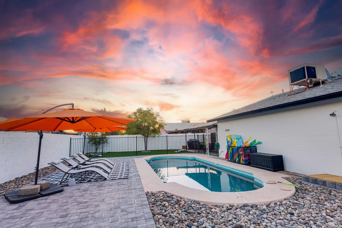 A vibrant outdoor pool scene with a swimming pool, a cheerful orange umbrella for shade, and a colorful mural as a fun backdrop. The setting is lively, hinting at sunny days spent swimming, sunbathing, or enjoying outdoor meals together.