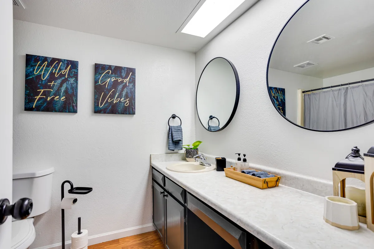 This image presents a modern vanity area with uplifting framed wall art, a round mirror, and a sink, radiating an uplifting and refreshing mood. The design suggests a soothing space for morning or evening routines, tying seamlessly into the en-suite bathroom feature mentioned.