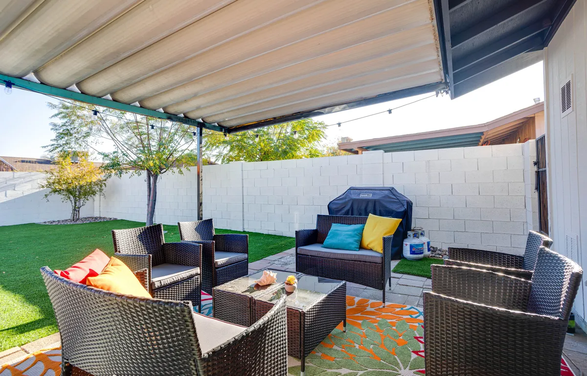 An inviting outdoor seating area with colorful cushions, a grill, and a decorative rug, all set against a relaxed backyard backdrop. The space is ideal for social gatherings, barbecues, and enjoying warm summer evenings outdoors.