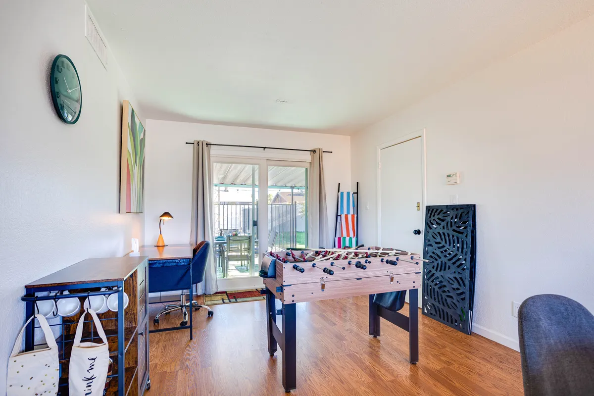A bright and inviting interior with a foosball table front and center, a sliding glass door offering access to outdoor space, and a modern desk and chair positioned for remote work or study. Wall art adds a playful touch, and the open layout encourages social interaction.
