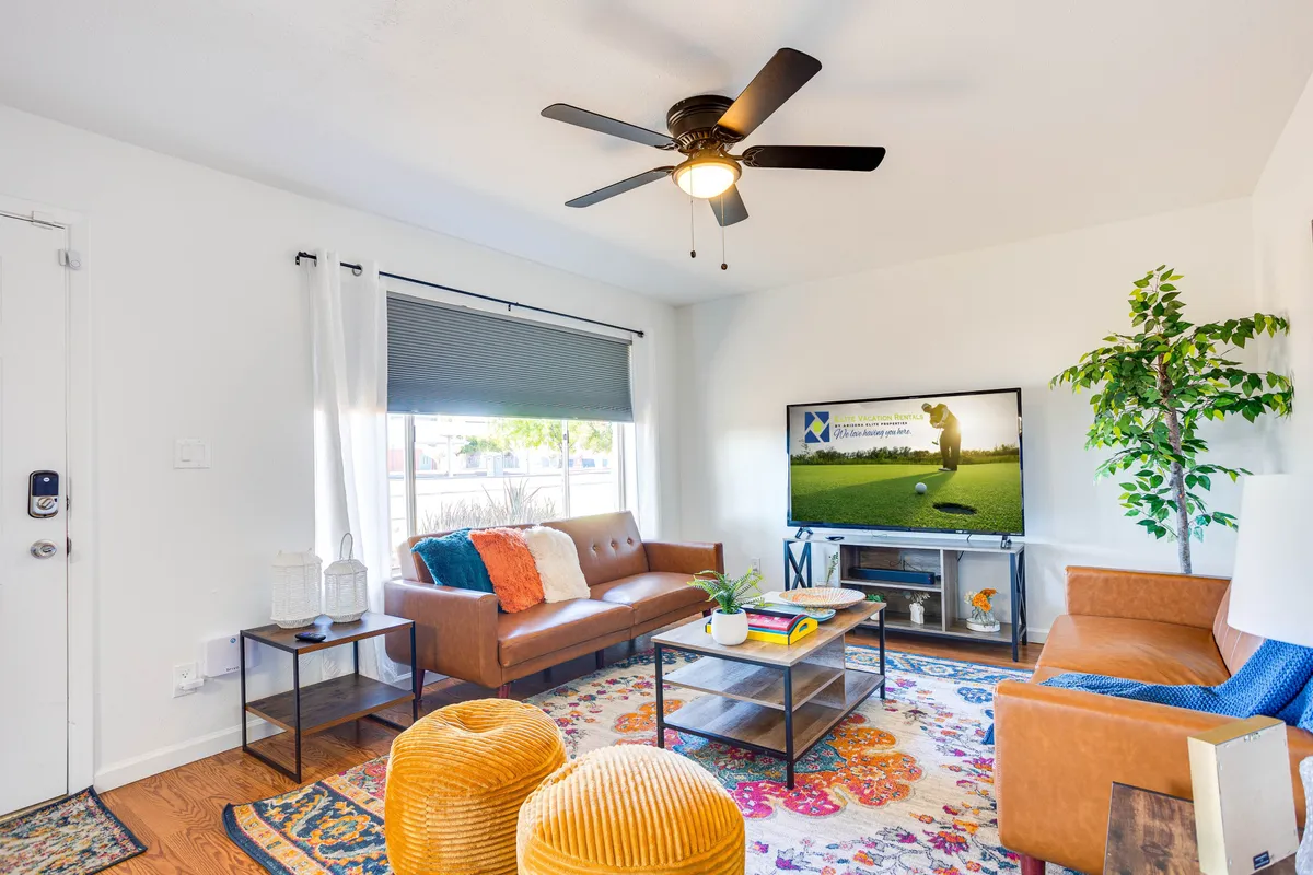 This image showcases a warm and welcoming living room featuring comfortable leather sofas, a colorful area rug, a large TV with visible content, and a potted plant. The layout is designed for family gatherings and relaxing together, with plenty of seating and entertainment options.