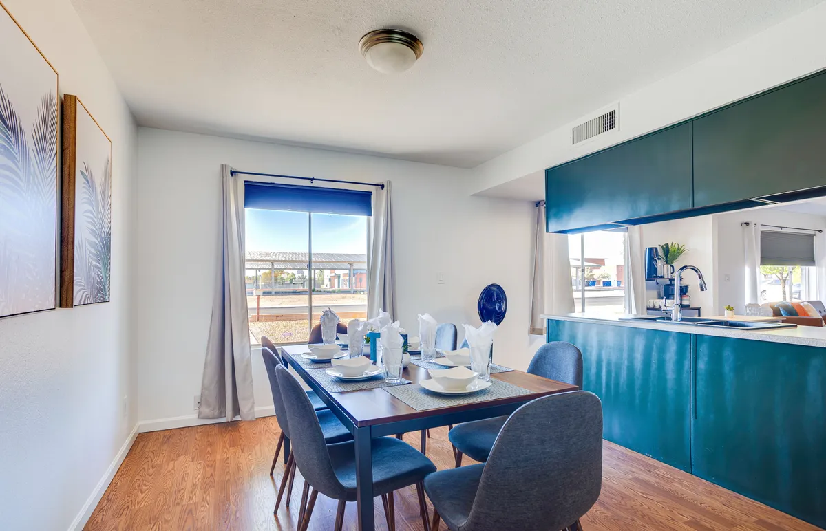 This interior image focuses on a dining table set for a meal with the kitchen area visible in the background. Ample natural light pours in through a large window, creating an inviting spot for family dinners and celebrations.