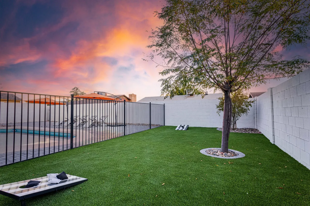 A tranquil backyard featuring a green lawn, a mature tree providing shade, and a fenced pool area. The scene suggests a peaceful, inviting outdoor space ideal for relaxation, social gatherings, or quiet moments in nature.