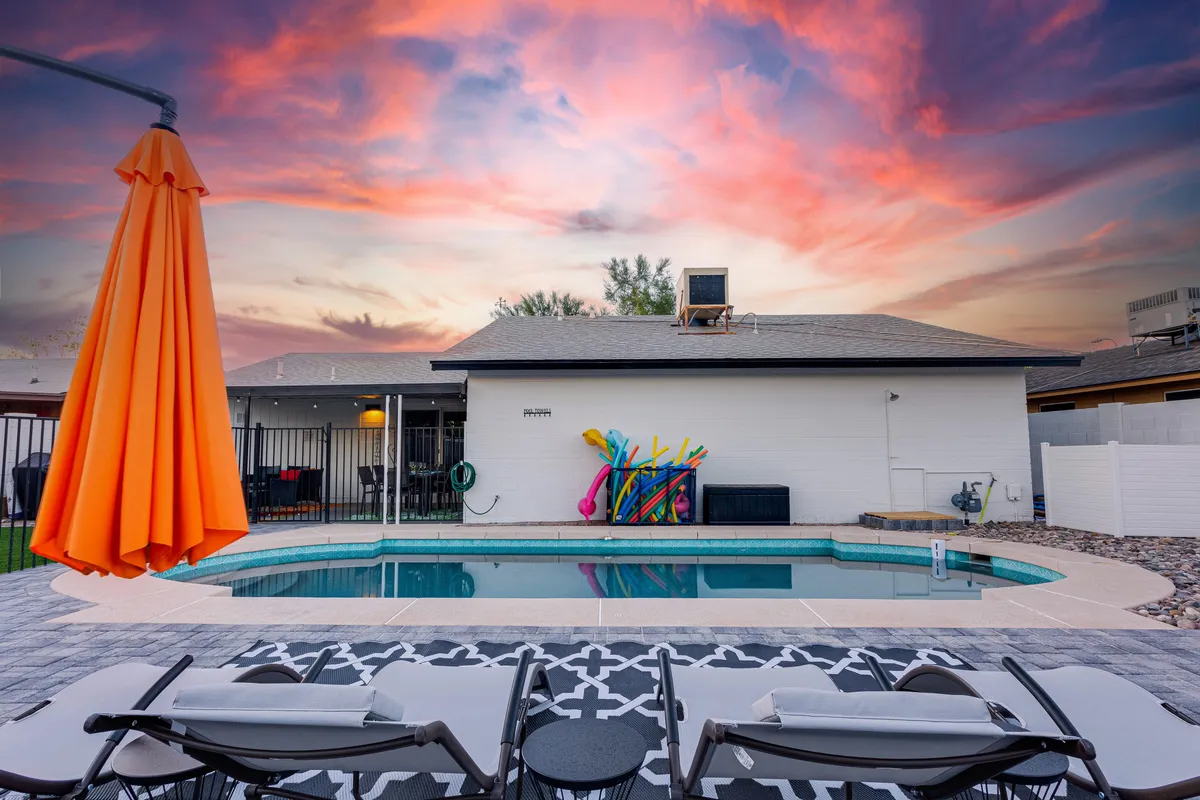 This image shows a sparkling swimming pool surrounded by lounge chairs, an orange umbrella for shade, and colorful pool toys scattered about. The scene exudes a playful, family-friendly vibe, perfect for both relaxation and active fun, with vibrant outdoor energy.
